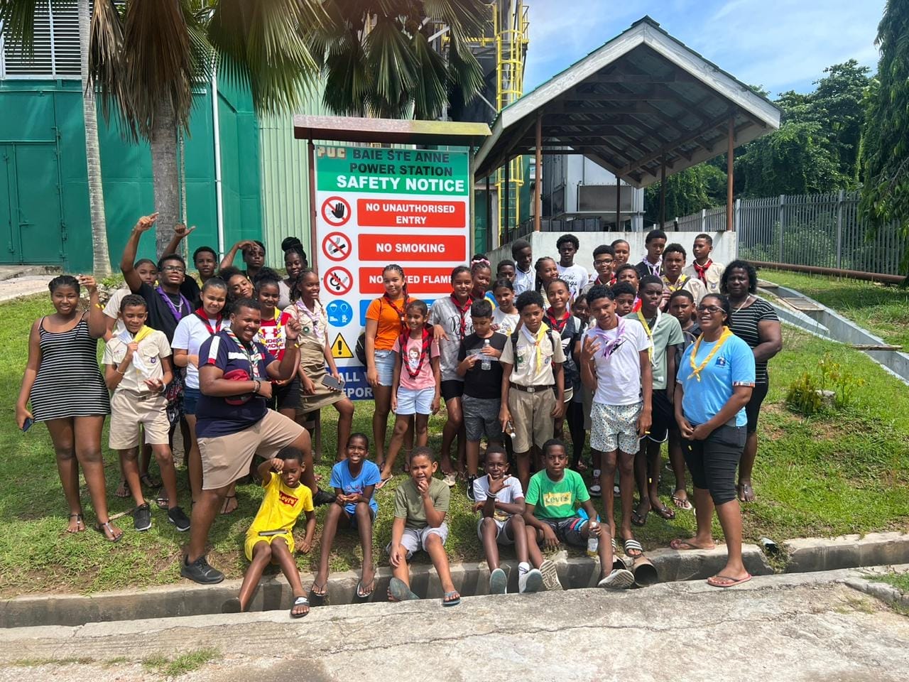 344904815_251883137342787_4747551511457726170_n Group photo of Seychelles Scout Association members with leaders, posing in front of the Baie Ste Anne Power Station safety notice sign during a field trip.