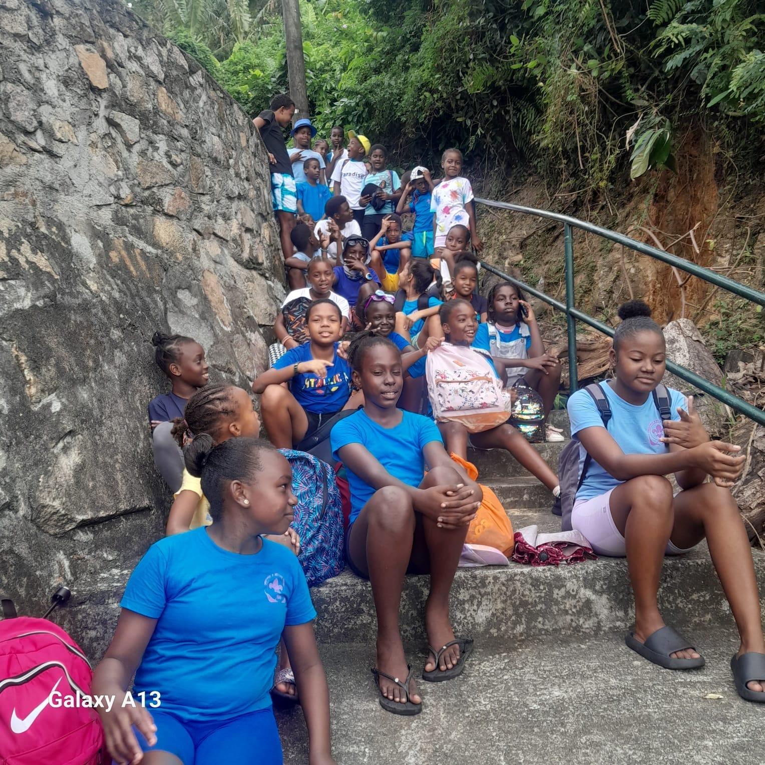 361197073_10233126833741528_7783325914869141349_n A group of young Seychelles Scouts in blue attire resting on stone steps during a hiking excursion, surrounded by lush tropical greenery.