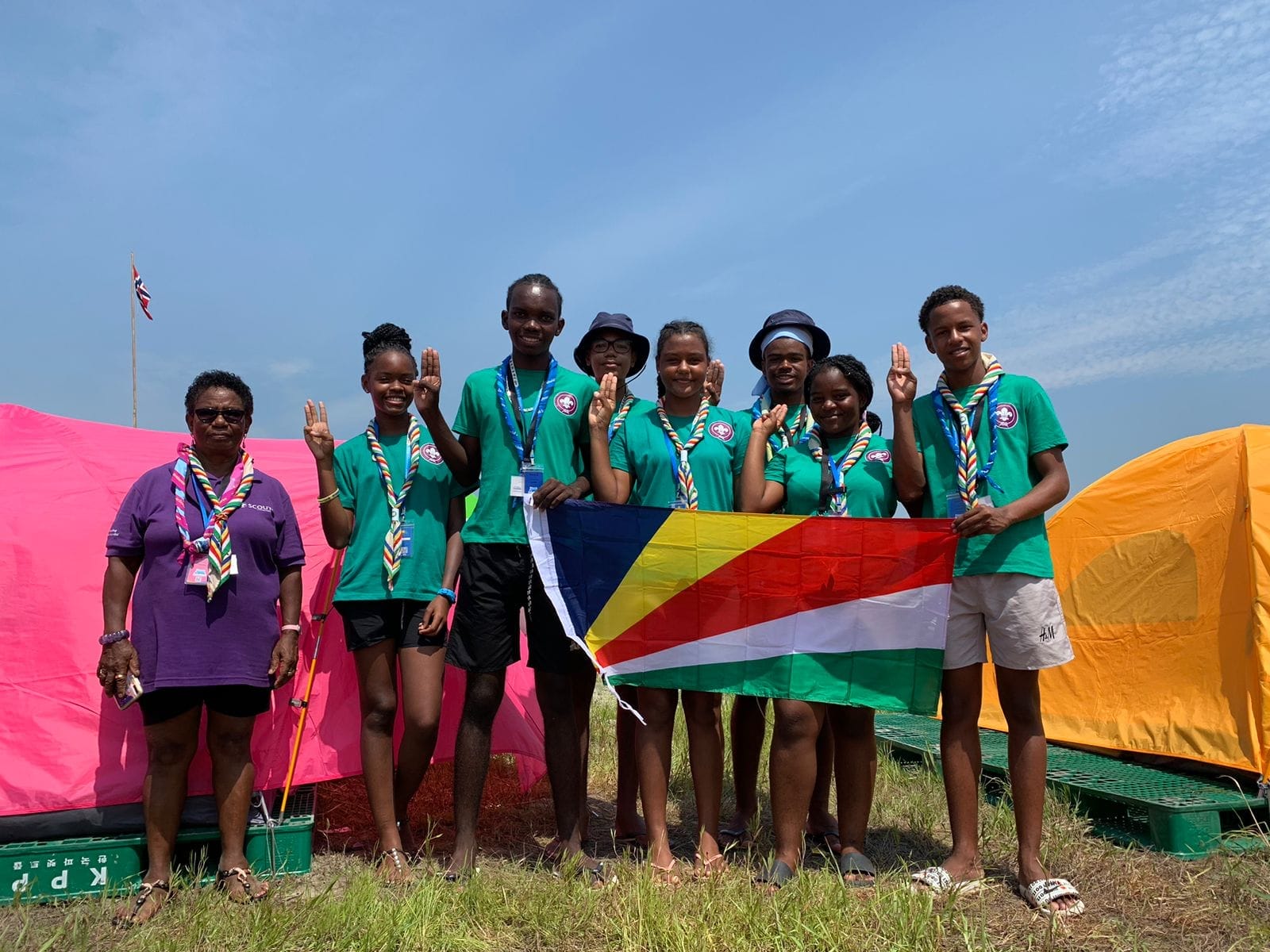 Seychelles Scouts proudly displaying the national flag with adult leaders at a campsite, symbolizing their commitment to scouting values and national pride.