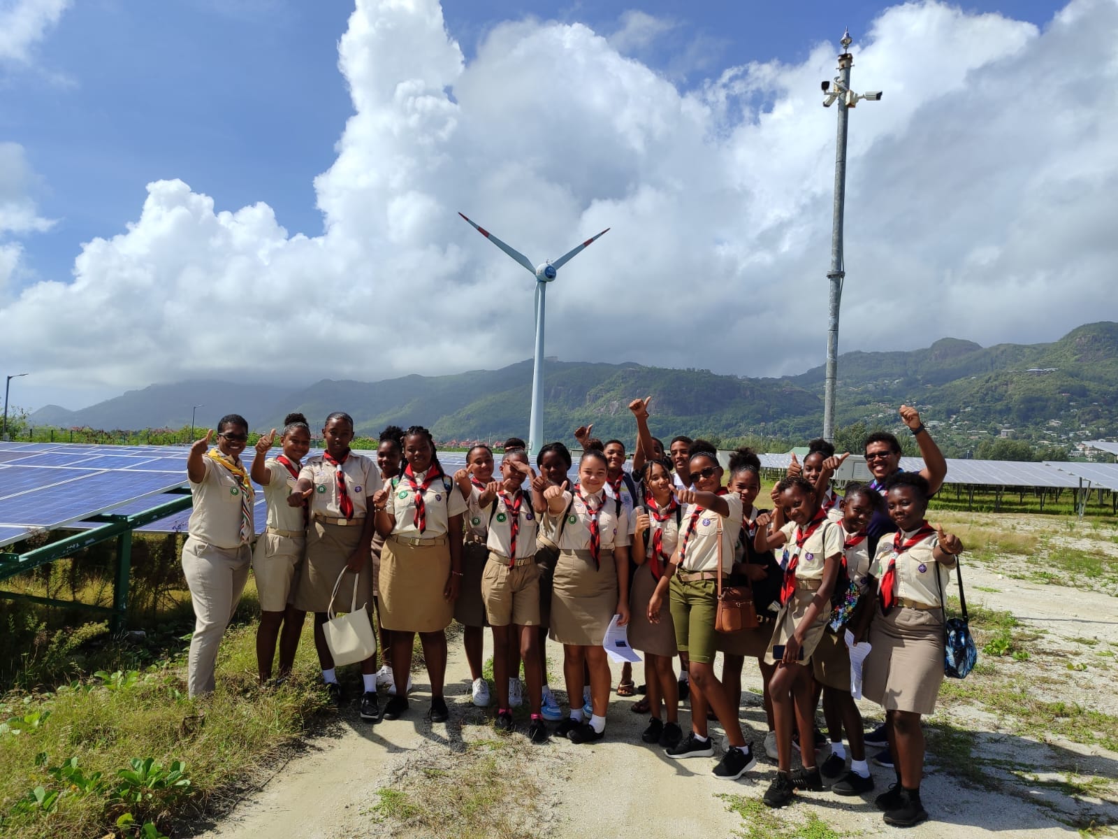 403838856_122125502036062808_5755597807677132525_n Energetic Seychelles Scouts group celebrating their visit to a renewable energy site with wind turbines and solar panels in the background, demonstrating their commitment to sustainability and green energy education.