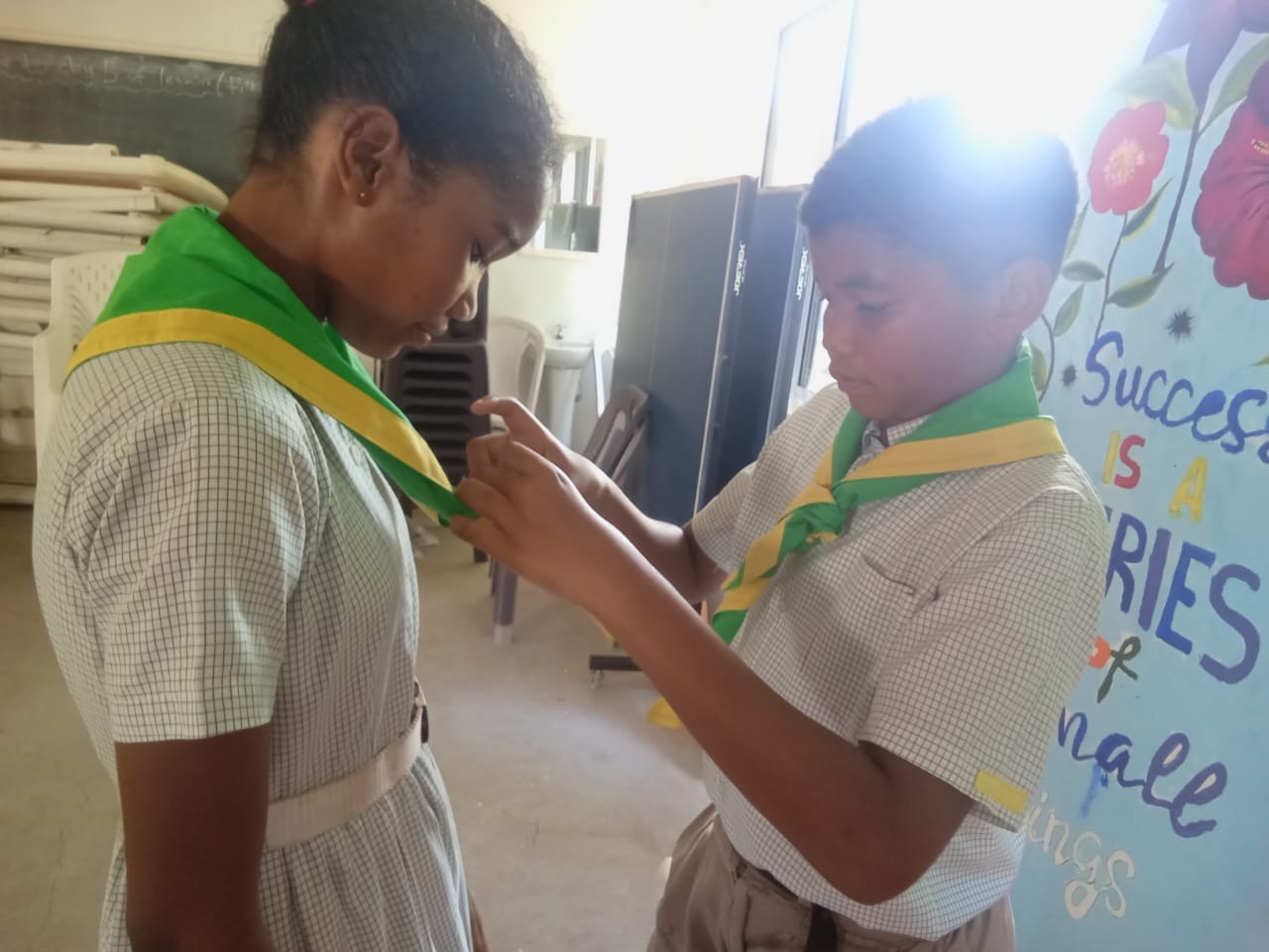407431708_122127056774062808_855593078986420518_n A boy scout pinning a badge on a boy scout's neckerchief in a classroom with educational posters, during a scout preparation activity.